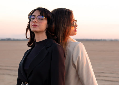 Two women standing back-to-back in a desert landscape at sunset.